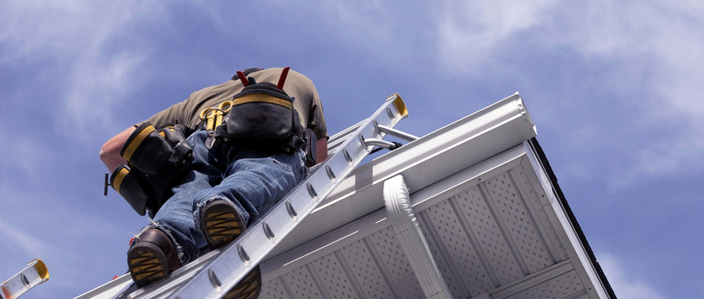 man on ladder resting on roof of house